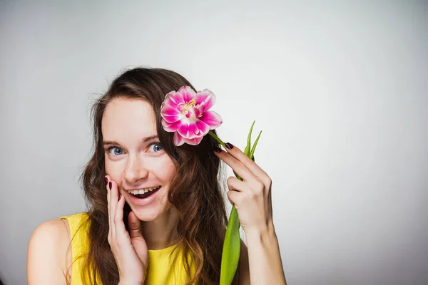 Glad ung kvinna ler, hålla i handen en doftande rosa blommor, firar den internationella kvinnodagen. 8 mars — Stockfoto