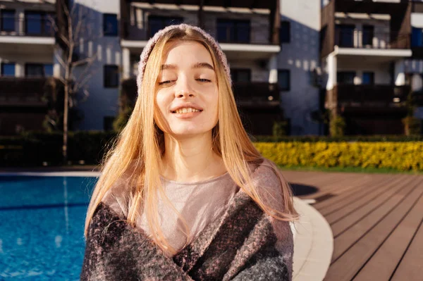 Feliz sorrindo menina loira em um chapéu rosa senta-se à beira da piscina azul, goza do sol e calor — Fotografia de Stock