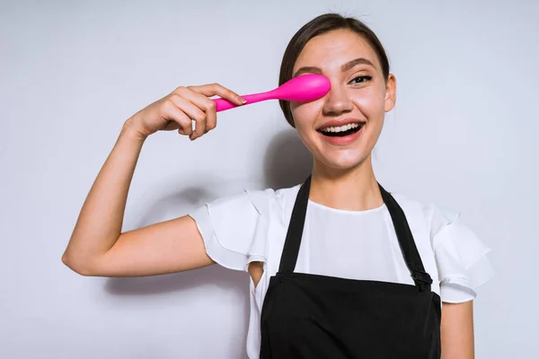 快乐的年轻妇女厨师在黑色围裙举行粉红色勺子近脸, 微笑 — 图库照片
