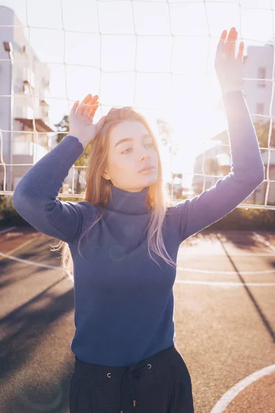 Stijlvolle mooi blond model meisje in blauwe trui poseren op sportveld, in de zon — Stockfoto