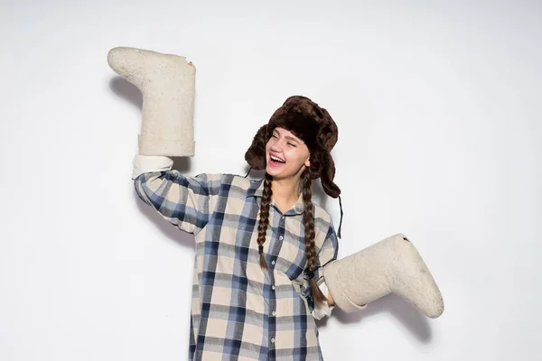 Fröhliches junges russisches Mädchen mit warmem Hut und Ohrenklappen hält Winterstiefel und lacht — Stockfoto
