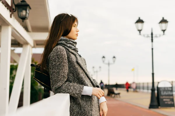 Stylish dark-haired young girl in a gray coat walking through the streets of the city, enjoying the overcast weather — Stock Photo, Image