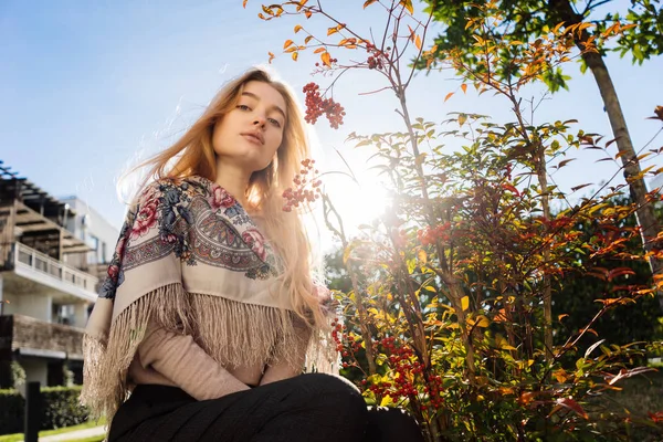 Jovem linda garota loira anda ao redor do jardim, em seus ombros um lindo lenço de cabeça, um dia quente de primavera e o sol — Fotografia de Stock