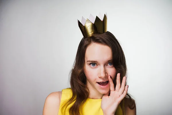 Divertida chica de ojos azules en un vestido amarillo está esperando el Día de la Madre, en su cabeza hay una corona de oro —  Fotos de Stock