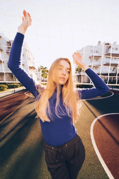 Mooie dunne blond model in een blauwe trui poseren op een sportveld in de zon — Stockfoto