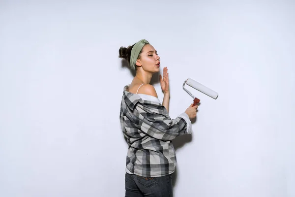 Jong meisje in oude shirt kleuren de muur met een roller platen in wit, doen van reparaties — Stockfoto
