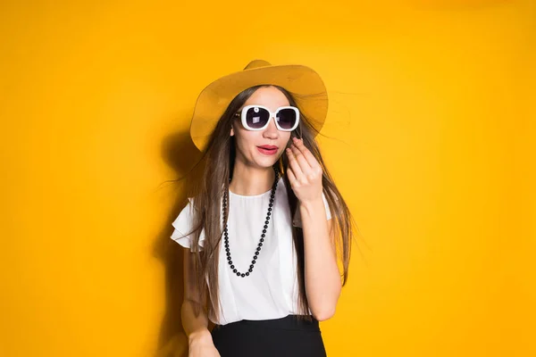 Bonito jovem modelo de menina de cabelos longos na moda chapéu grande e óculos de sol posando no fundo amarelo — Fotografia de Stock