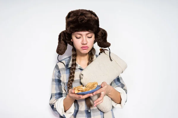 Ein junges russisches Mädchen mit warmem Pelzhut hält heiße Pfannkuchen in der Hand, feiert Fastnacht — Stockfoto