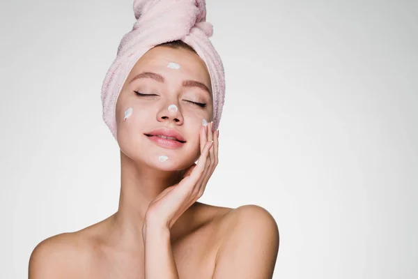 Beautiful young girl with a pink towel on her head applying moisturizer on face — Stock Photo, Image