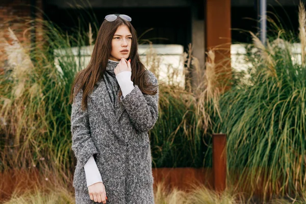 Una chica de la ciudad de pelo oscuro con estilo en un abrigo gris camina por las calles de la ciudad, piensa en algo — Foto de Stock