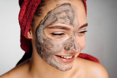 mutlu genç kız başında kırmızı bir havlu ile uygulanan bir kil maskesi yüzü gülüyor