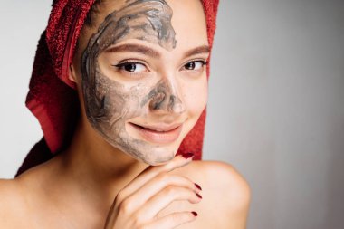 başında kırmızı bir havlu ile çok hoş bir gülümseyen kız yararlı kil maskesi yüzünde, uygulanan Spa gün