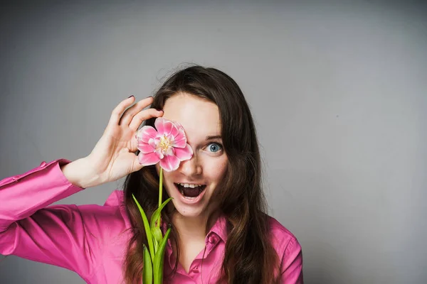 Pembe gömlekli mutlu sürpriz genç kadın kokulu bir çiçek tutan, 8 Mart Dünya Kadınlar günü kutluyor — Stok fotoğraf