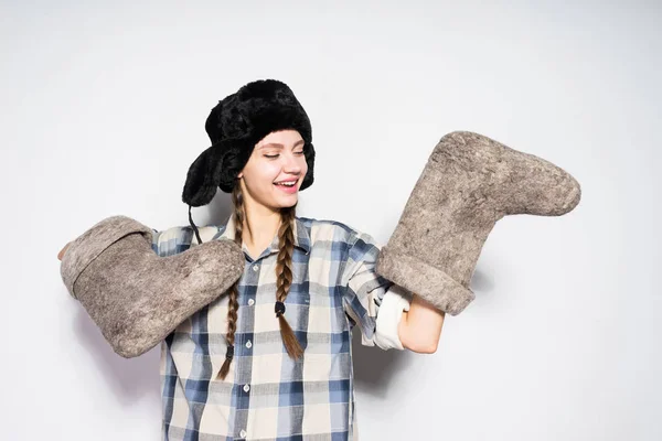 Glückliche junge russische Mädchen mit einem warmen Hut hält ein Paar Winterstiefel — Stockfoto