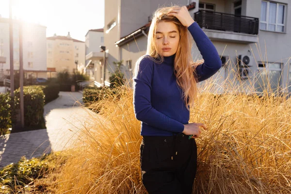 Bela menina loira elegante em suéter azul goza de clima quente e luz do sol, estilo de rua, passeios pela cidade — Fotografia de Stock