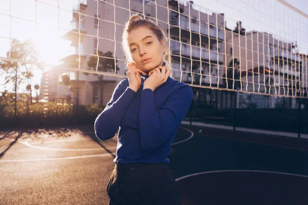Zeker mooi stijlvolle meisje model in een blauwe trui poseren op een sportveld in de zon — Stockfoto