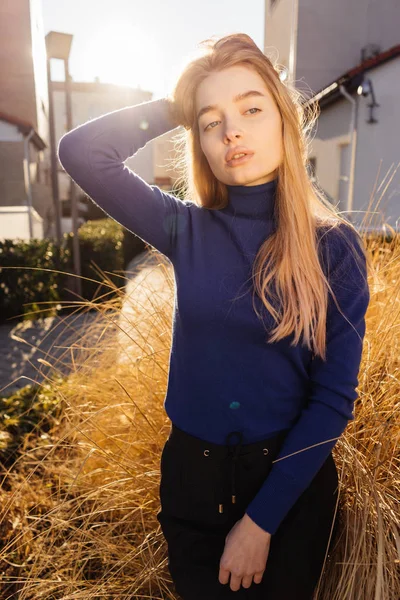 Stylish confident young blond girl in blue sweater strolls through the city streets in the sun — Stock Photo, Image