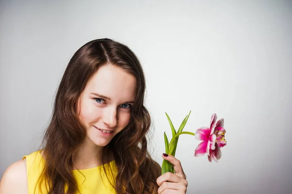 Krásná mladá blue-eyed dívka v žlutých šatech drží růžový květ, čekání na den žen světa — Stock fotografie