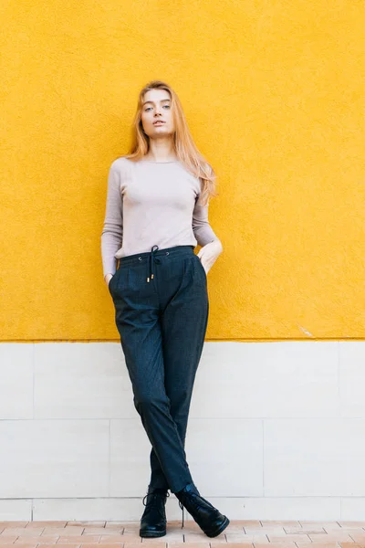 Slanke stijlvolle mooi blond meisje poseren tegen een gele muur achtergrond, straat mode en stijl — Stockfoto