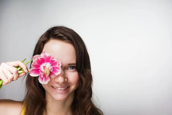 Šťastná mladá žena držící růžový květ v blízkosti obličeje, úsměvu, slaví Den matek — Stock fotografie