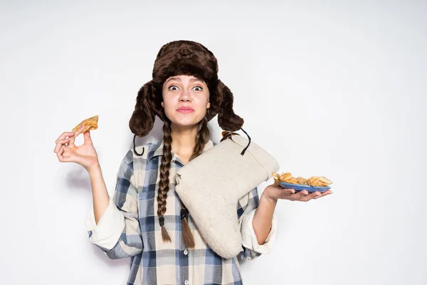 Grappig jonge Russische meisje in een warme muts, warme pannenkoeken eten en vieren stuk — Stockfoto