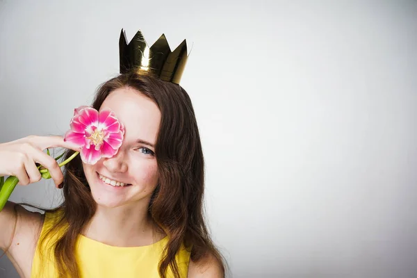 Hermosa joven sosteniendo una flor rosa cerca de su cara, con una corona de oro, esperando el día mundial de la mujer — Foto de Stock