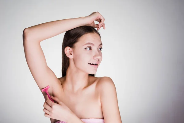 Beautiful young girl shaves her hair on her armpits with a razor, after a shower — Stock Photo, Image