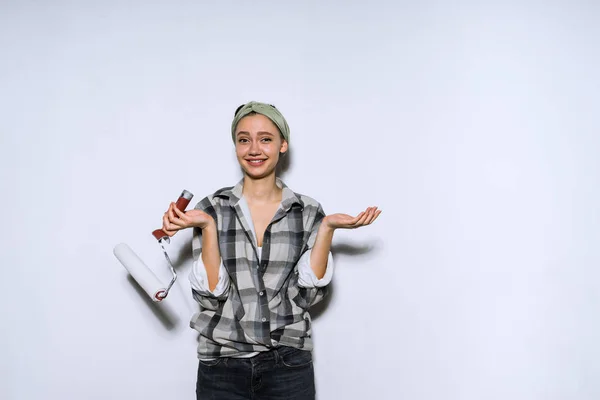 Linda chica divertida en una camisa sosteniendo un rodillo para pintar la pared, haciendo reparaciones — Foto de Stock