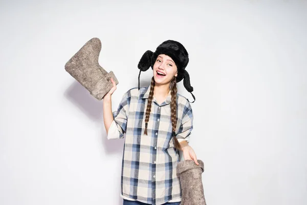 Smějící se krásná Ruská dívka drží teplé zimní cítil boty, kožešinovou čepici na hlavu — Stock fotografie