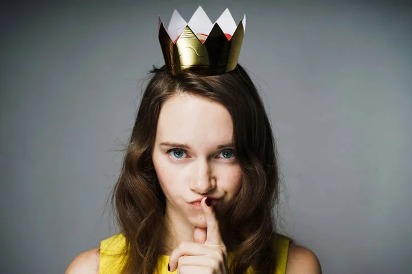 Hermosa hermosa chica de ojos azules en un vestido amarillo puso un dedo en sus labios, una corona en su cabeza — Foto de Stock