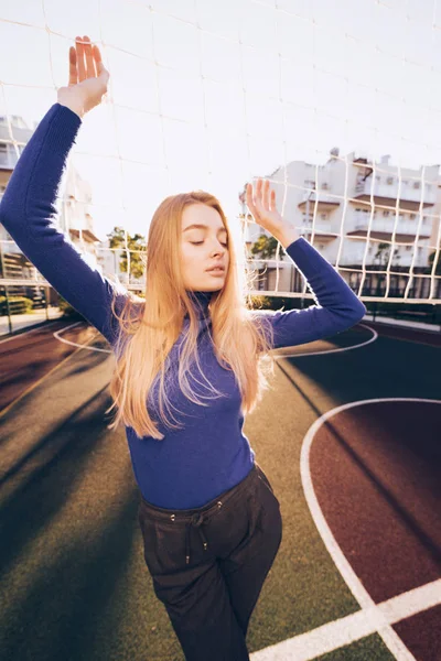 Stijlvolle jong blond meisje in blauwe trui poseren op sportveld — Stockfoto