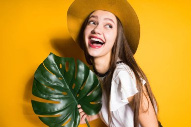 trendy şapkalı kız mutlu uzun saçlı genç model yeşil bir yaprak, gülüyor ve pozlar tutar