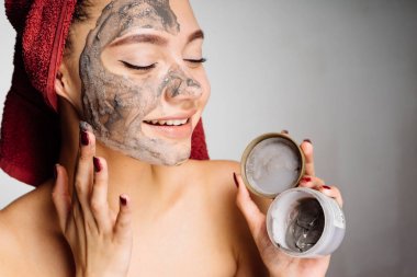 Kafasındaki bir havlu ile mutlu sevimli kız bir yararlı kil maskesi yarım yüzüne koyar.