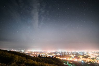 dağların eteklerinde büyük bir şehir, parıldayan ve parlar, birçok fenerler, gece yıldızlı gökyüzü altında