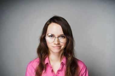 Kendine güvenen genç kadın pembe gömlek ve gözlük gülümsüyor ve çalışmaları hakkında düşünüyor