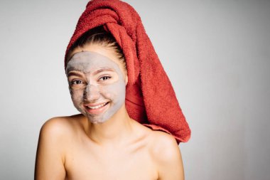 başında kırmızı bir havlu ile genç kız gülümseyerek, bir yararlı yüzünü maske, günlük bakım koymak