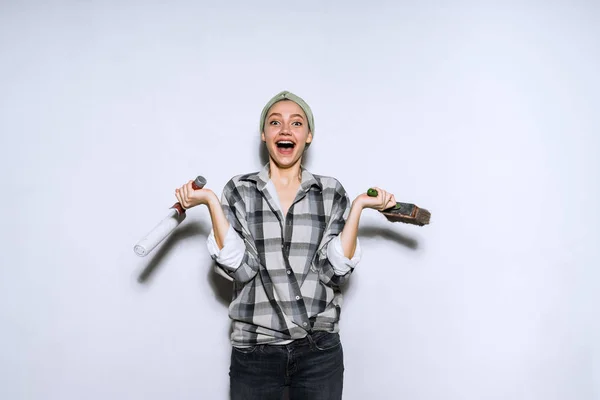 Счастливая смеющаяся молодая девушка в клетчатой рубашке держа в руках роллер и кисть для покраски стен — стоковое фото