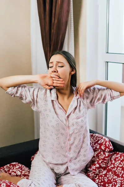 Schläfriges junges Mädchen im rosa Pyjama wacht früh auf, gähnt und will nicht aufstehen — Stockfoto