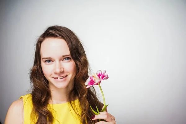 Menina feliz no vestido amarelo, de olhos azuis, mantém a flor rosa, celebra o dia das mulheres do mundo — Fotografia de Stock