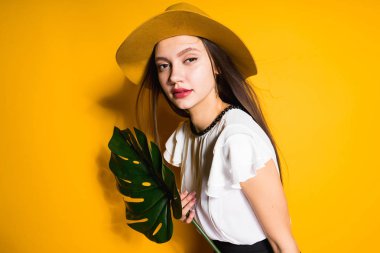 genç çekici uzun saçlı kız moda şapkalı bir yaprak yeşil, sarı bir arka plan üzerinde poz tutar