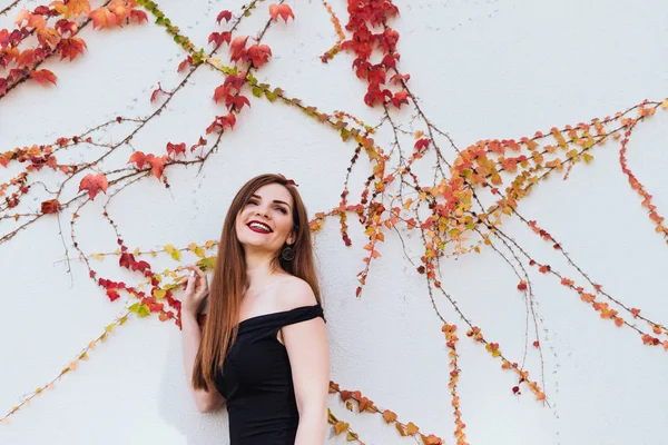 Skrattande långhåriga Ursnygg flicka i en svart klänning som går runt hennes trädgård, poserar mot väggen — Stockfoto