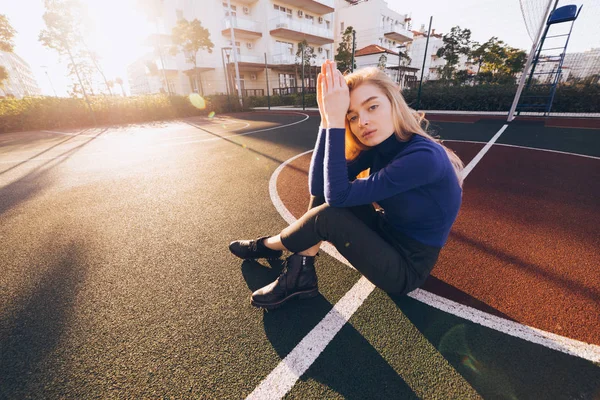 Elegante jovem loira modelo menina em suéter azul posando no campo de esportes no sol da manhã — Fotografia de Stock