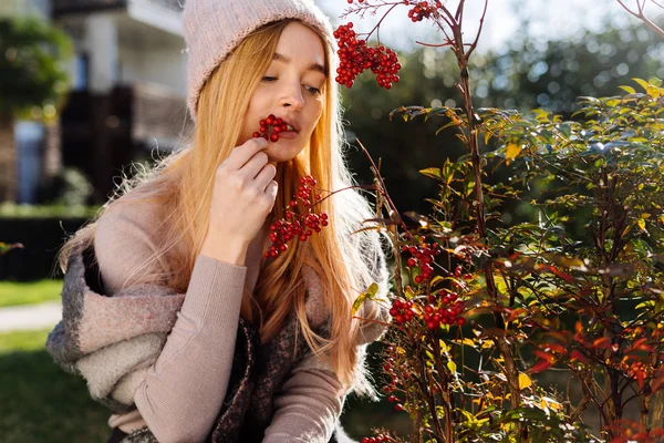 Giovane bella ragazza bionda con un cappello rosa passeggiando in giardino, provando le bacche sul palato — Foto Stock