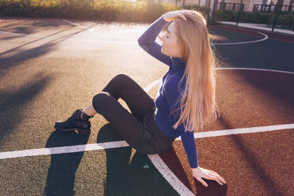 Stylisches langhaariges Model im blauen Pullover sitzt auf einem Spielplatz in den Strahlen der Morgensonne — Stockfoto