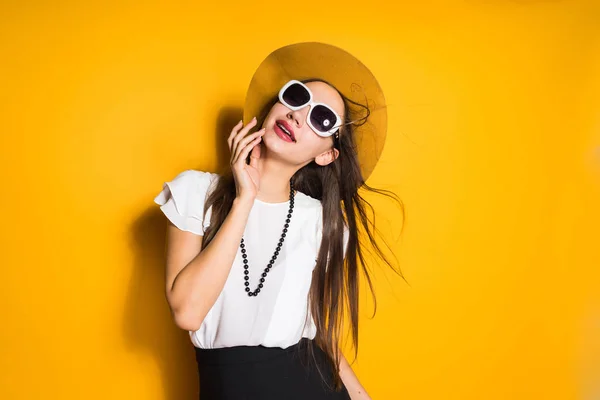 Atraente modelo de menina de cabelos longos em chapéu preto e óculos de sol posando no fundo amarelo — Fotografia de Stock