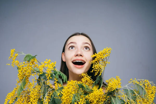 Mujer feliz entre las pequeñas flores amarillas mira hacia arriba, 8 de marzo, día de la mujer — Foto de Stock