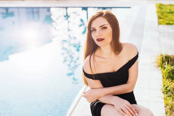 Όμορφη, πλούσια γυναίκα κάθεται στο φόντο της πισίνας, υπόλοιπο — Φωτογραφία Αρχείου