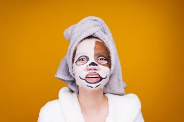 Kafasındaki bir havlu ile şaşkın bir kadının yüzünde bir köpeğin namlu şeklinde nemlendirici maske uygulamak