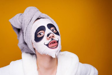 bir havlu başında afallamış bir kadınla bir panda bir namlu şeklinde yüzünde bir nemlendirici maske uygulamak