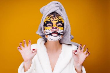Kafasındaki bir havlu ile mutlu kadın yüzünde bir kaplanın namlu şeklinde bir nemlendirici maske uygulamak